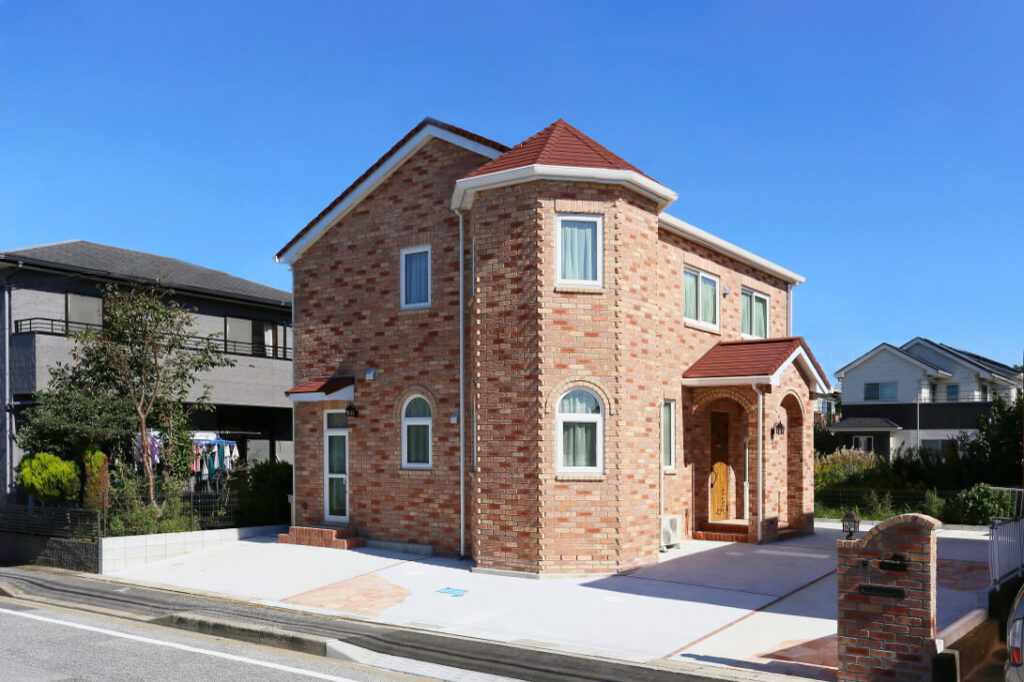 中世のお城のような優美なレンガ積みの家の塔屋とピンク系のレンガが目を引く外観